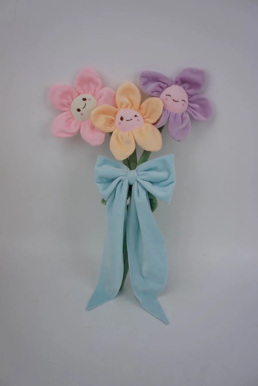 Plush colourful fabric in the shape of 3 stemmed flowers with playful faces secured by a large bow